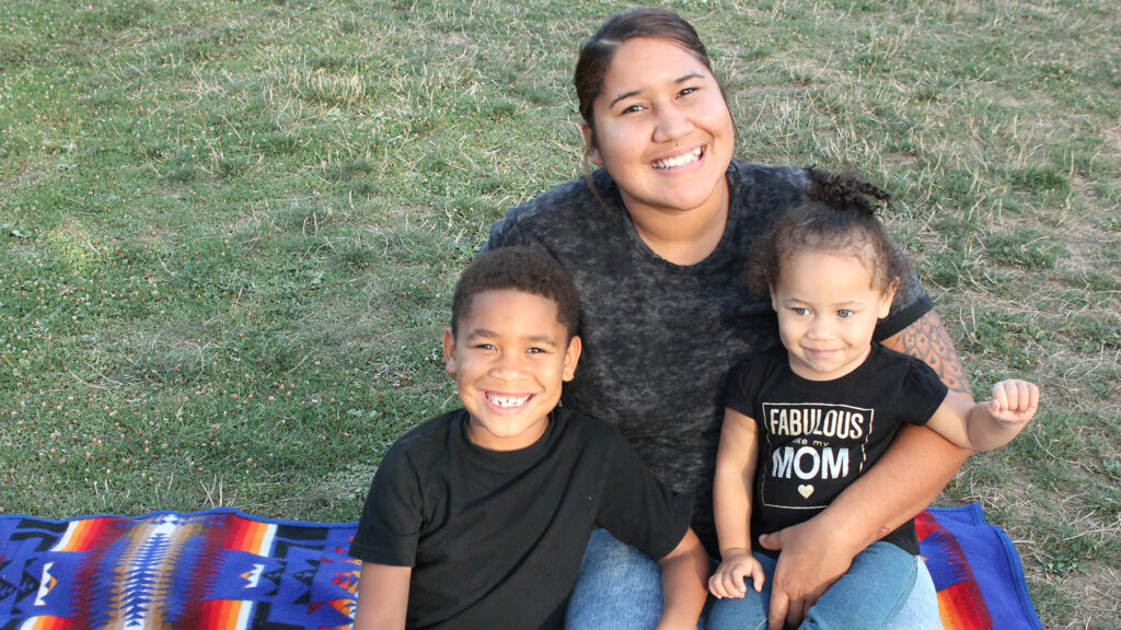 Mother and young son and daughter sit on a picnic blanket.