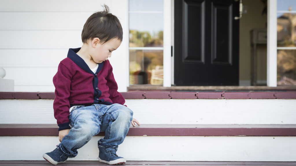 Small child sits on porch steps alone and looks at empty space beside him.