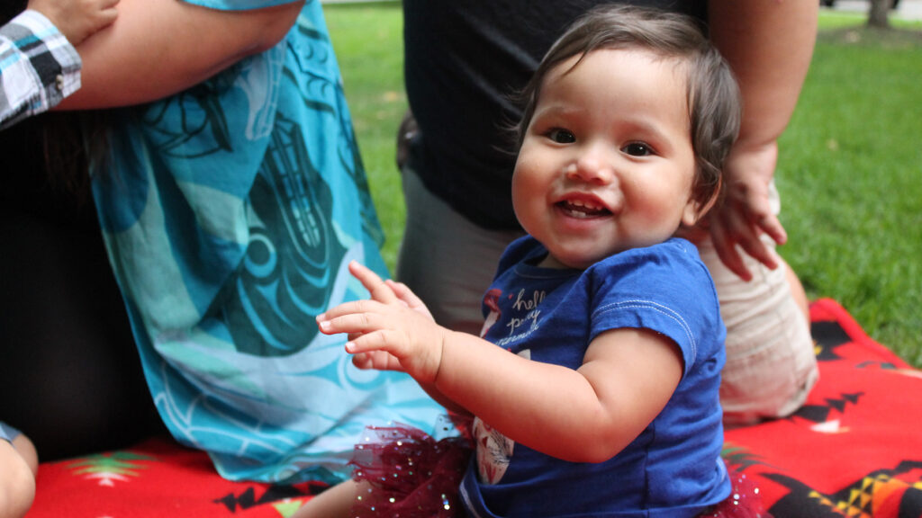Toddler smiling at camera with parents in background.